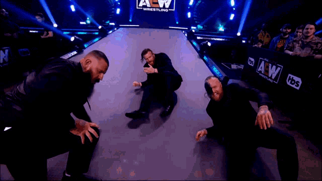 a group of men are kneeling on a wrestling ring with a tbs logo in the background