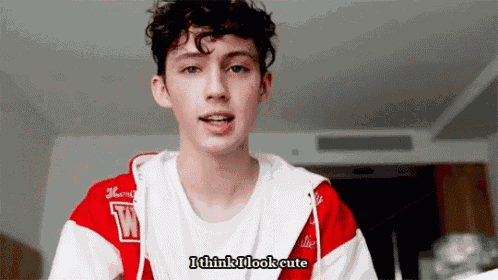 a young man with curly hair is wearing a red and white jacket that says i think i look cute