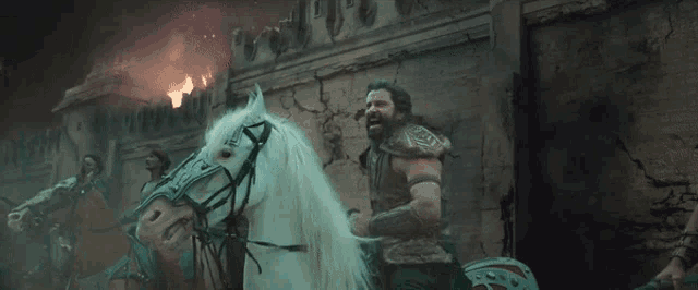 a man riding a white horse in front of a fire