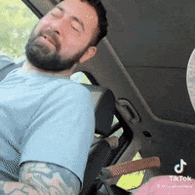 a man with a beard and tattoos is sleeping in the back seat of a car .