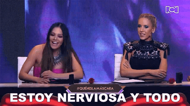 two women sit at a table with a sign that says estoy nerviosa y todo on it