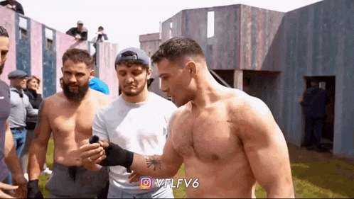 a group of men are standing next to each other without shirts and one of them has a tattoo on his arm .