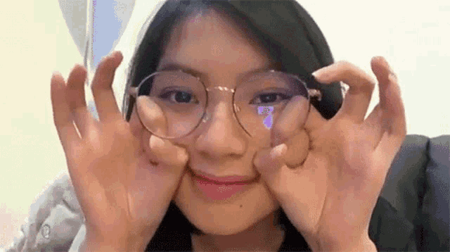 a young woman wearing glasses is making a funny face with her hands .