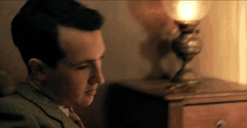 a man in a suit sits in front of a lamp on a table