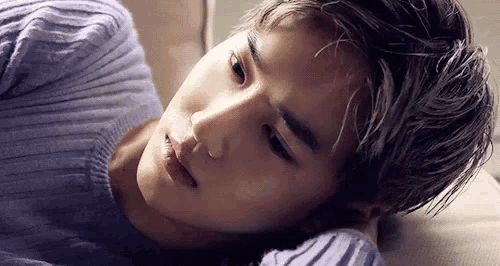 a young man in a purple sweater is laying on a bed with his head on a pillow .