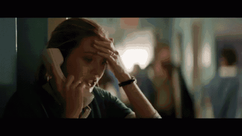 a woman holds her head while talking on a telephone