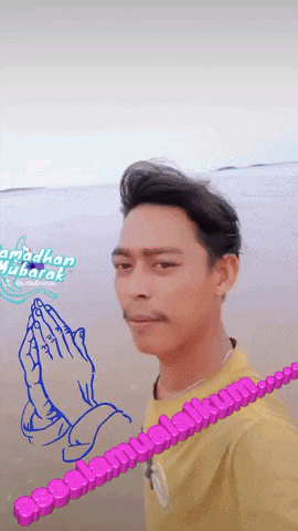 a man in a yellow shirt is standing on a beach with a drawing of praying hands behind him