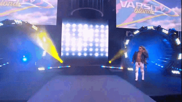 a man is walking down a stage with varsity blondes written on the screen behind him