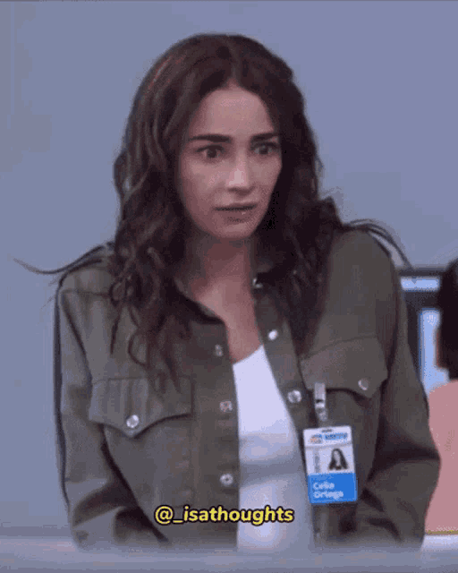 a woman wearing a green jacket and a name tag that says @isathoughts
