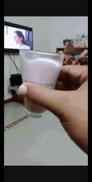 a person is holding a glass of liquid in front of a tv