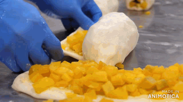 a person in blue gloves is spreading yellow slices on a piece of dough