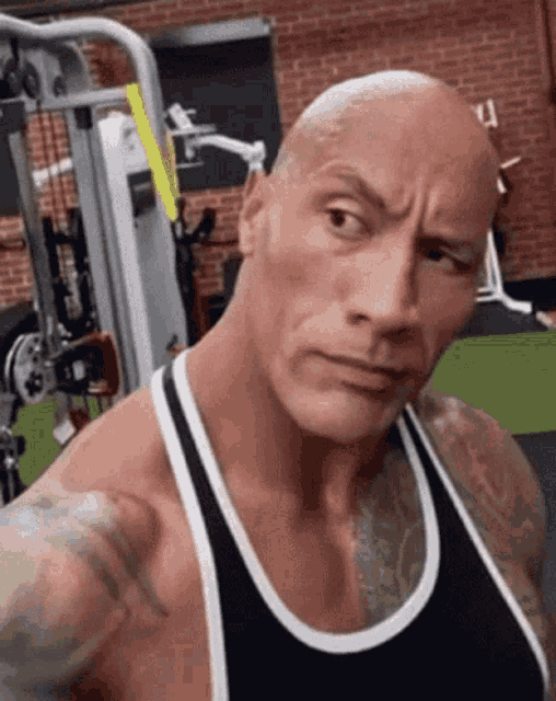 a bald man in a tank top is standing in a gym and pointing at the camera .