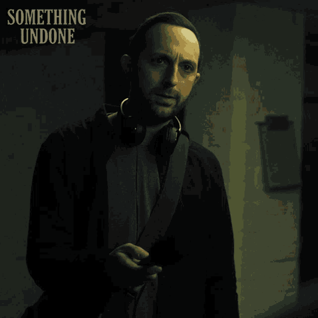 a man wearing headphones stands in front of a sign that says something undone