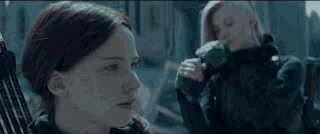 two women are standing next to each other in a dark room and one has a shaved head