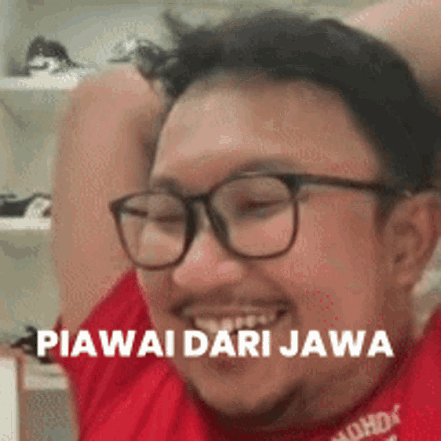 a man wearing glasses and a red shirt with the words piawai dari jawa written on it .