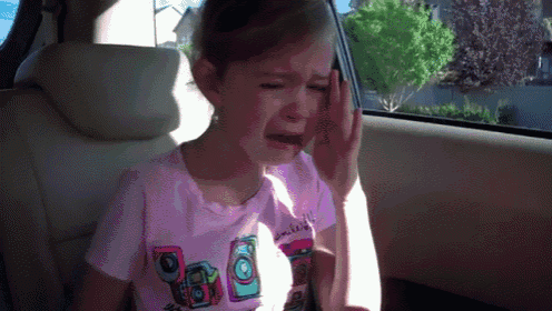 a little girl is crying in the back seat of a car while wearing a pink shirt with a camera on it