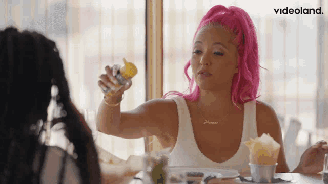 a woman with pink hair is sitting at a table with a videoland logo in the corner