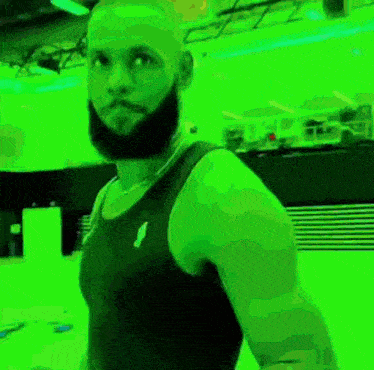 a man with a beard wearing a black tank top is standing in front of a green background .
