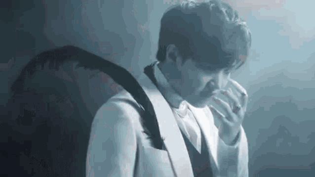 a man in a white suit with black feathers on his wings is holding his nose .