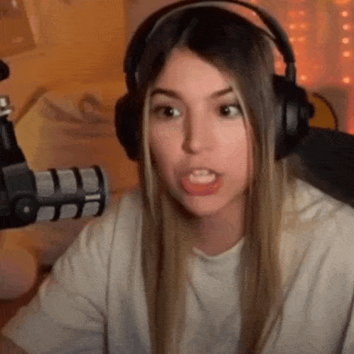 a woman wearing headphones and a white shirt is sitting in front of a microphone .