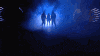 a blurry picture of a group of people standing in a dark room with a blue light behind them .