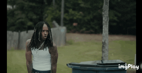 a man with dreadlocks is standing next to a trash can with imgplay written in the corner