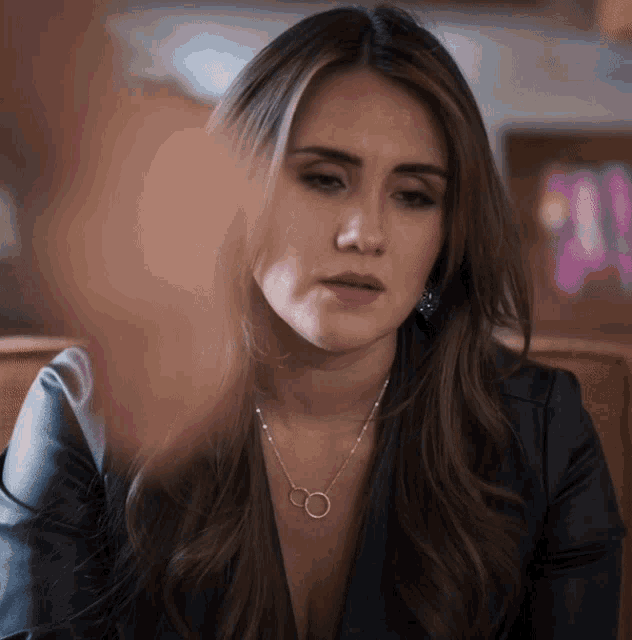 a woman wearing a black jacket and a silver necklace with two circles on it