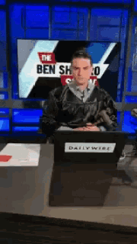 a man is sitting at a desk in front of a screen that says the ben show