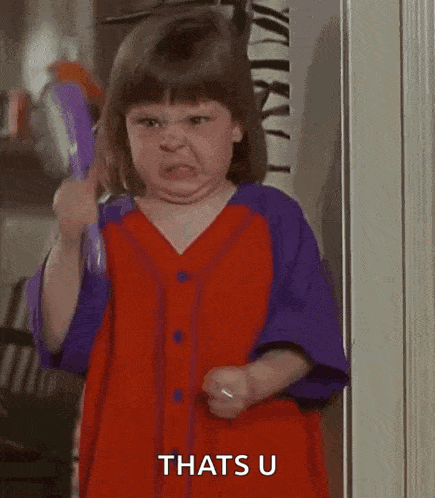 a little girl in a red and purple dress is holding a comb and making a funny face .