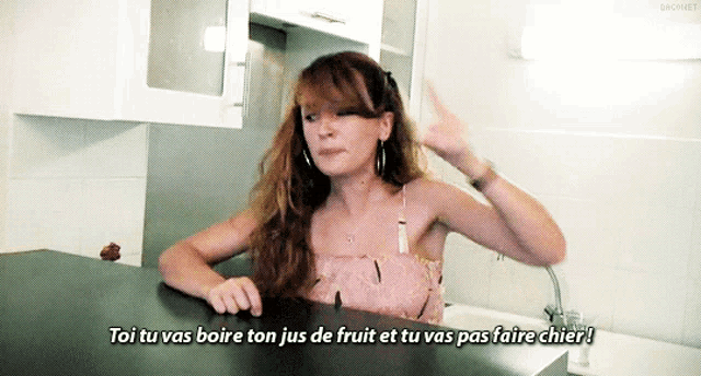 a woman sitting at a kitchen counter says toi tu vas boire ton jus de fruit and tu vas pas faire chier
