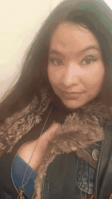a woman wearing a denim jacket with a fur collar is smiling