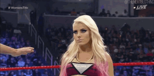 a blonde woman is standing in a wrestling ring with a crowd watching .
