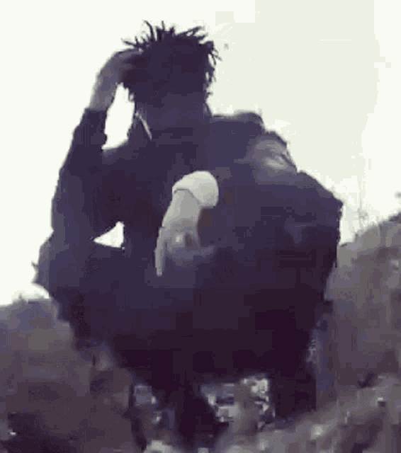 a man with dreadlocks is sitting on a rock holding a cigarette in his hand .