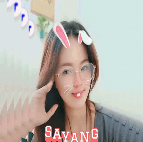 a woman wearing glasses and bunny ears has the word sayang in red