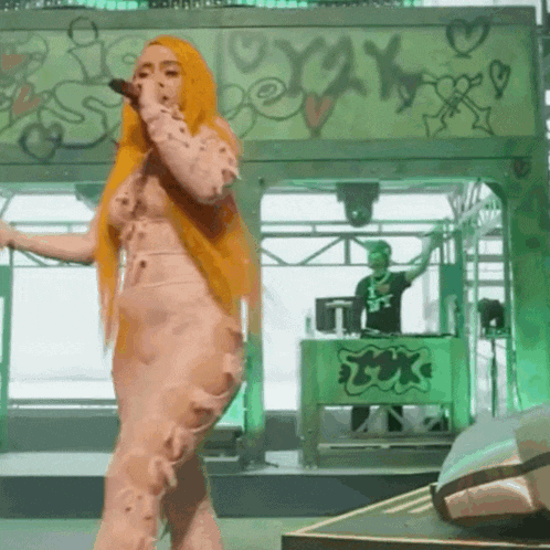 a woman with orange hair singing into a microphone in front of a green wall that has the word oxy on it
