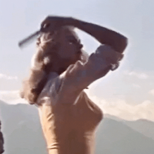 a woman is holding a knife over her head while standing in front of a mountain .