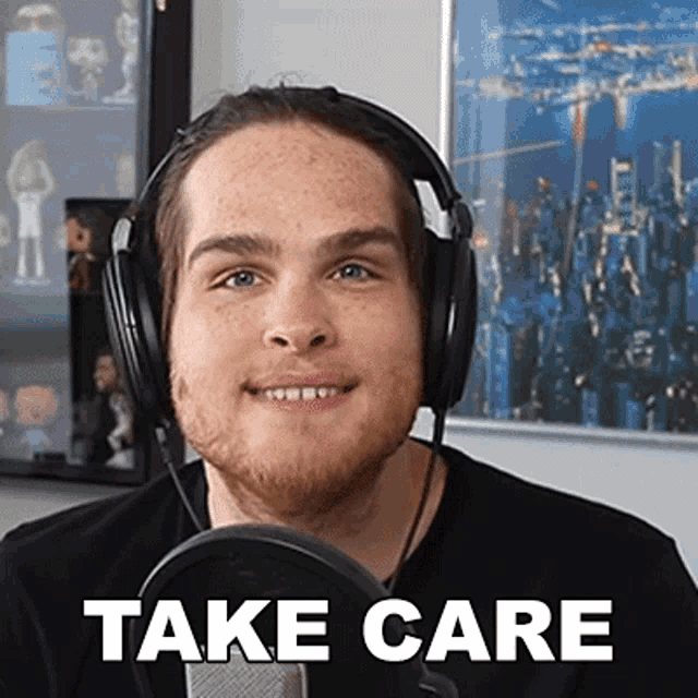 a man wearing headphones is smiling in front of a microphone and the words take care are on the screen behind him .