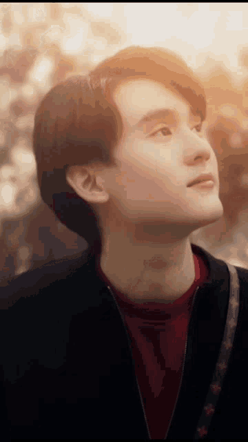 a young man in a red shirt and black jacket looks up at the sky