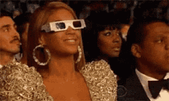 a woman wearing 3d glasses is smiling while sitting in a crowd .