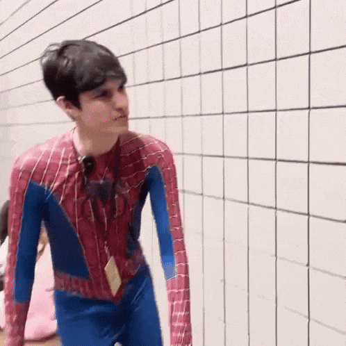 a man in a spiderman costume is standing in a hallway holding a hat .
