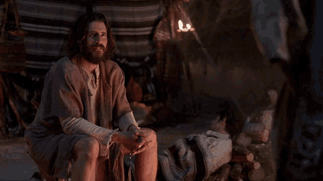 a man with a beard is kneeling down in front of a fire