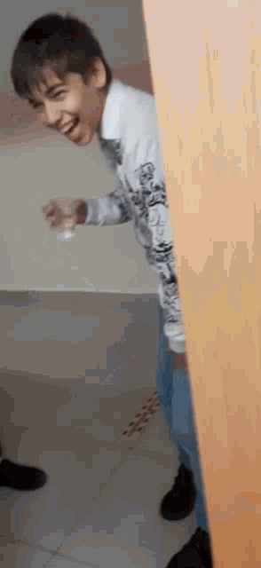 a boy is standing behind a door holding a glass of water .