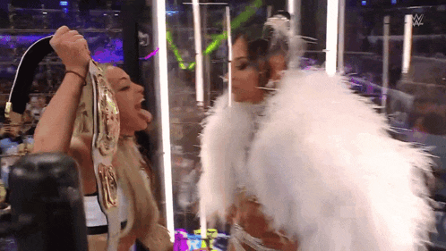 a woman in a white feathered outfit holds a wrestling championship belt