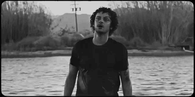 a black and white photo of a man standing in front of a body of water .
