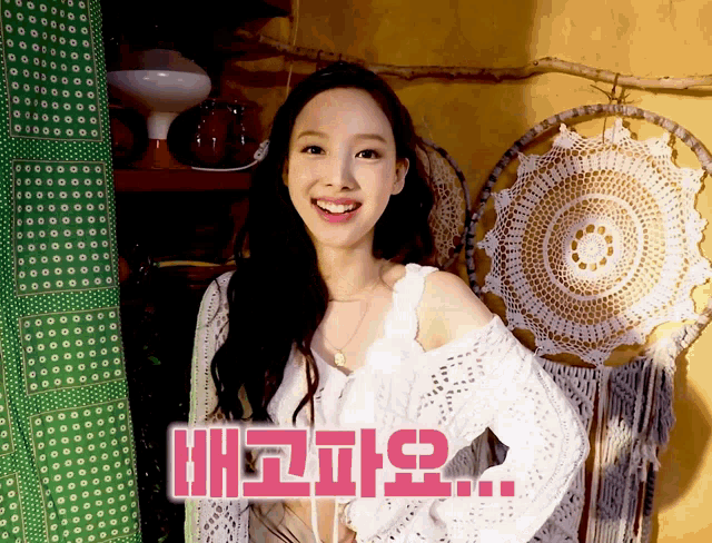 a woman in a white sweater smiles in front of a wall with crocheted circles on it