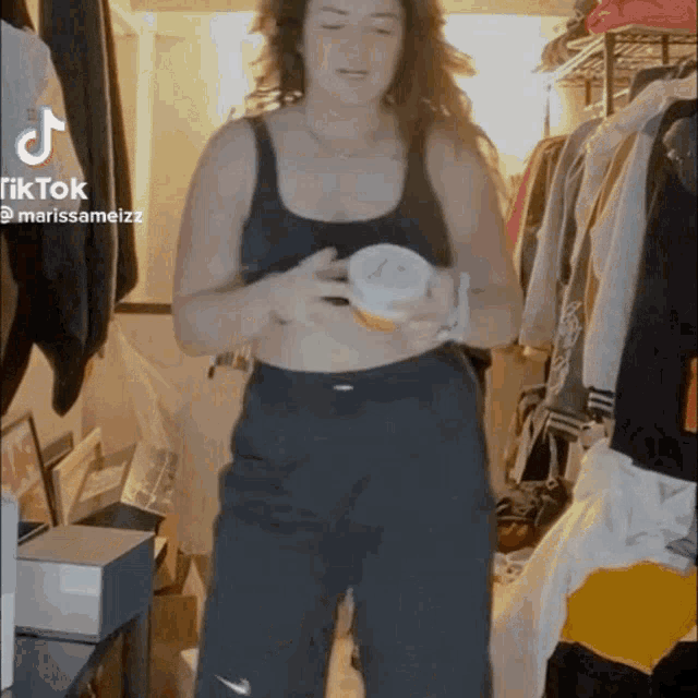 a woman in a black tank top and black pants is standing in a room holding a cup .