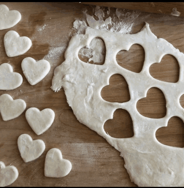 heart shaped cookies are cut out of dough on a wooden surface
