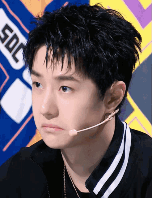 a young man wearing a microphone looks at the camera