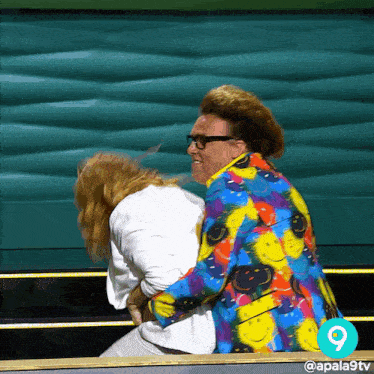 a man in a colorful jacket holds a woman in a white shirt