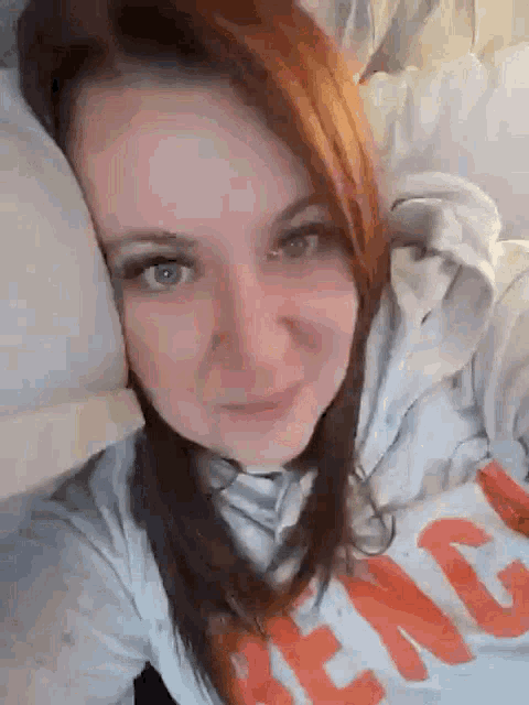 a woman with red hair is laying on a bed with her head on a pillow and smiling .